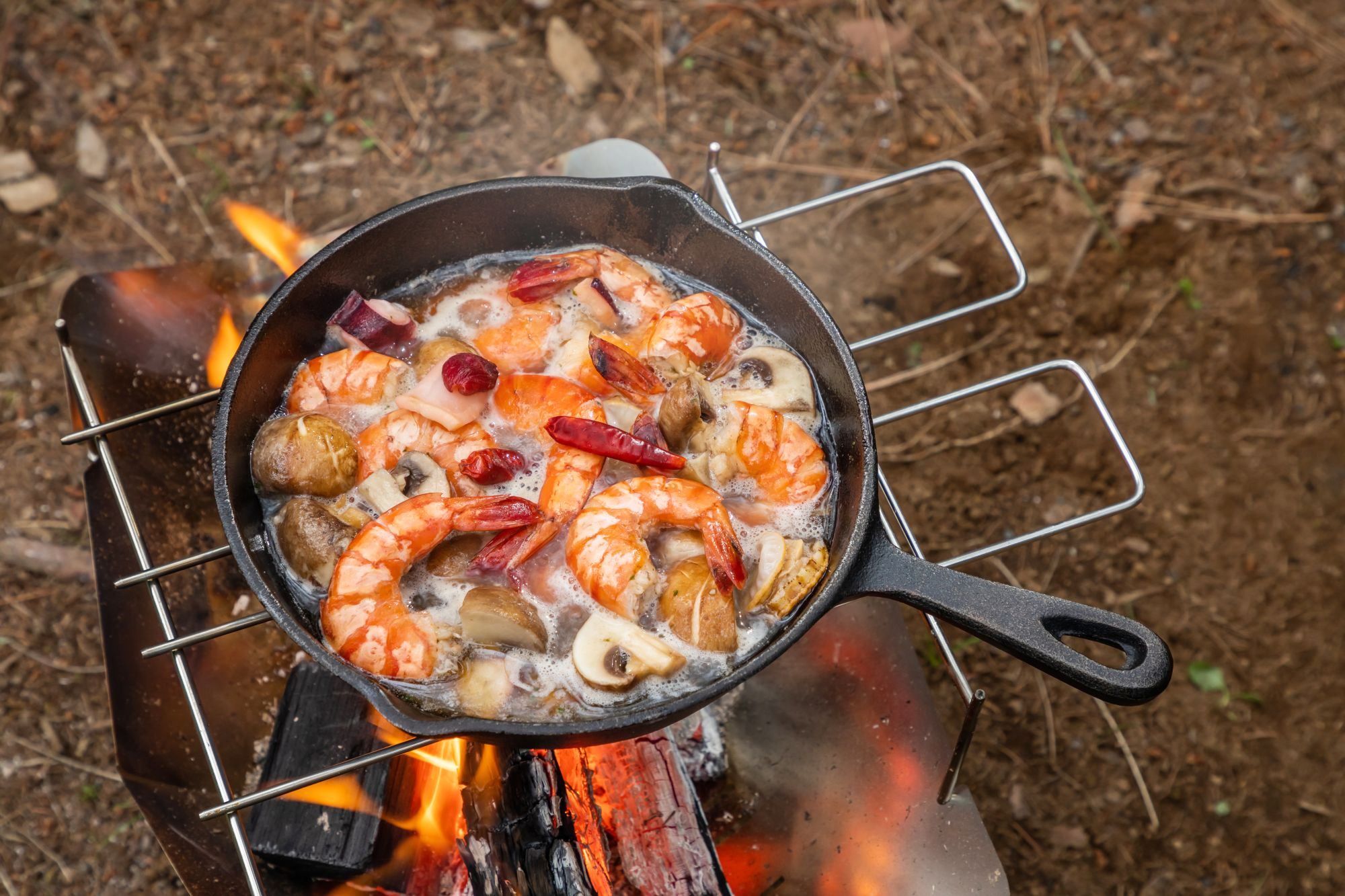 cast iron pan over a campfire cooking shrimp and mushrooms