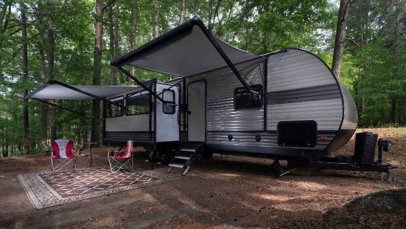 A camper trailer in the woods with both awnings extended