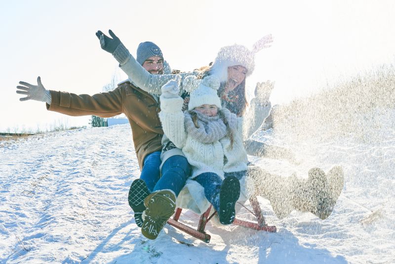 A mother, father, and daughter sledding down a snowy hill